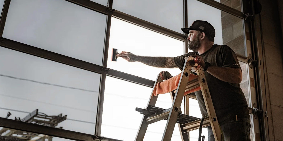 Man standing on ladder installing flat glass window film